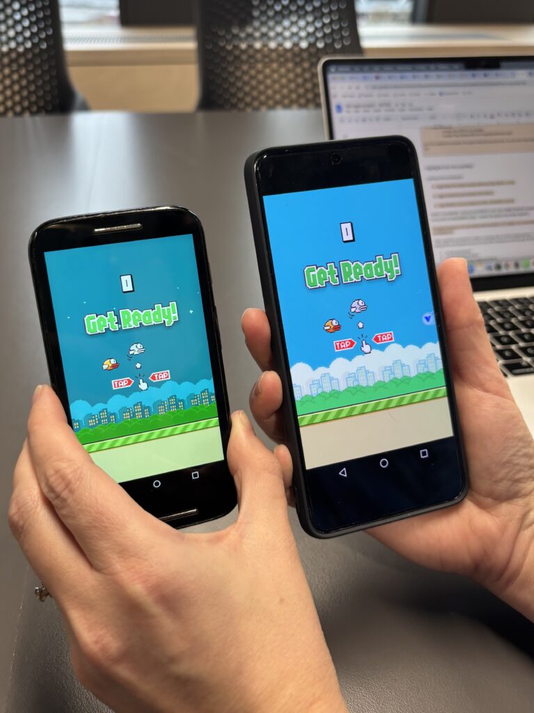 Two mobile phones displaying Flappy Bird. The first is a phone from the launch of Flappy Bird, with the app installed directly. The colours are more muted than on the later phone model, which is running the game through an emulator app.